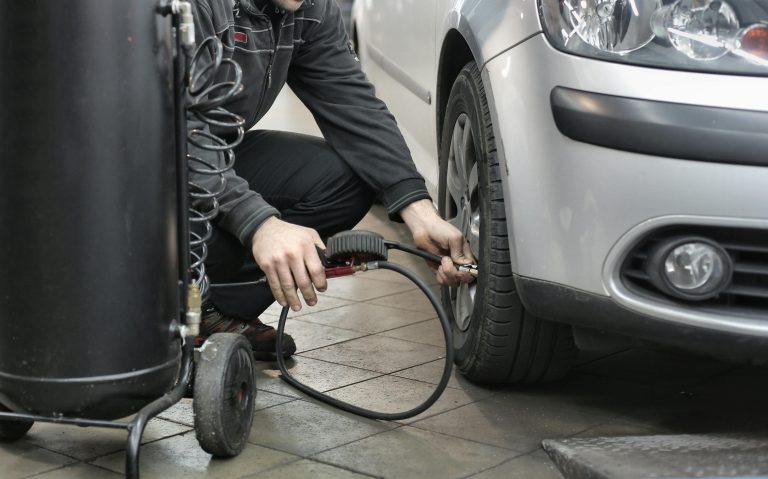 Close-up of a man checking tyre pressure and inflating a car tyre.